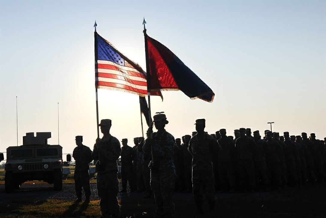 soldiers stand in a formation with two flags