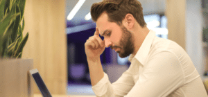 a man sits at his computer thinking with his hand on his head