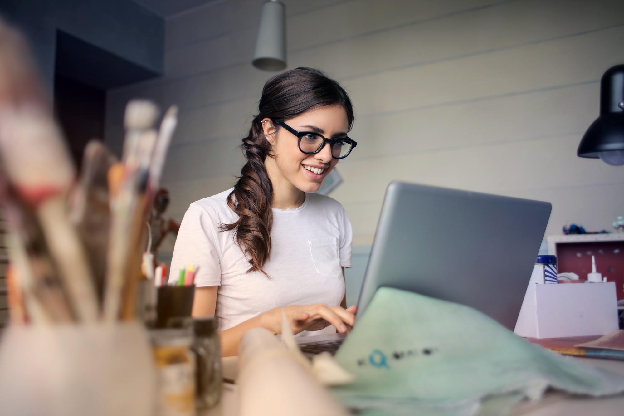 a girl wearing glasses smiles as she works on a computer