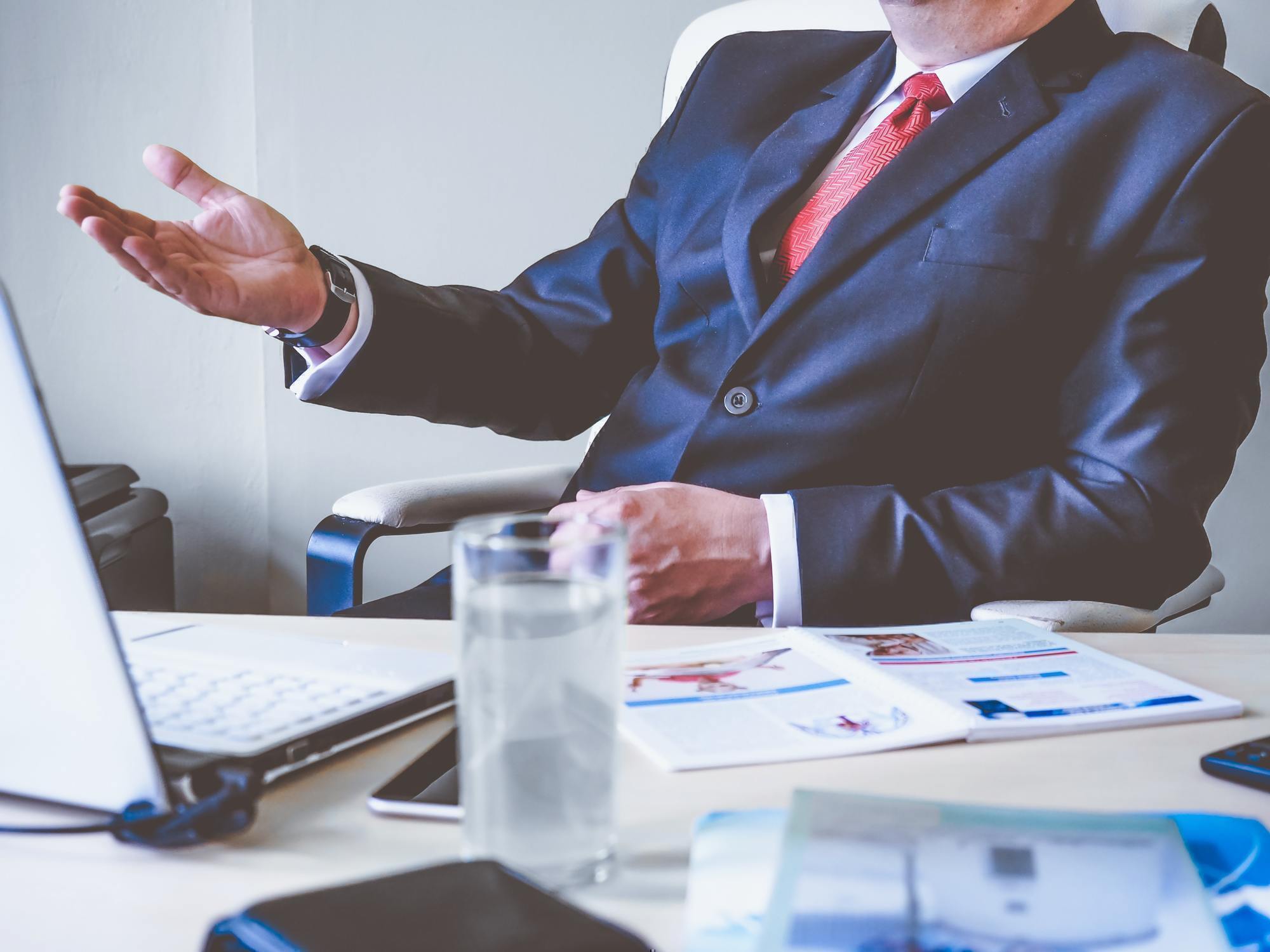 a man wearing a suit talks across a desk