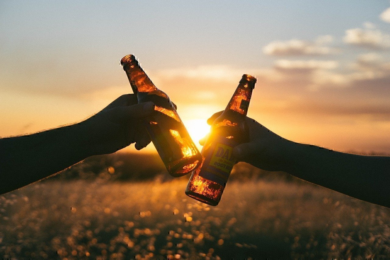 two people tap bottles of beer together in the sunset