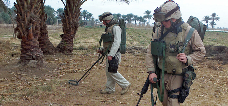 two soldiers scanning for explosives on a dirt trail