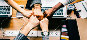 five people bump their fists over a desk