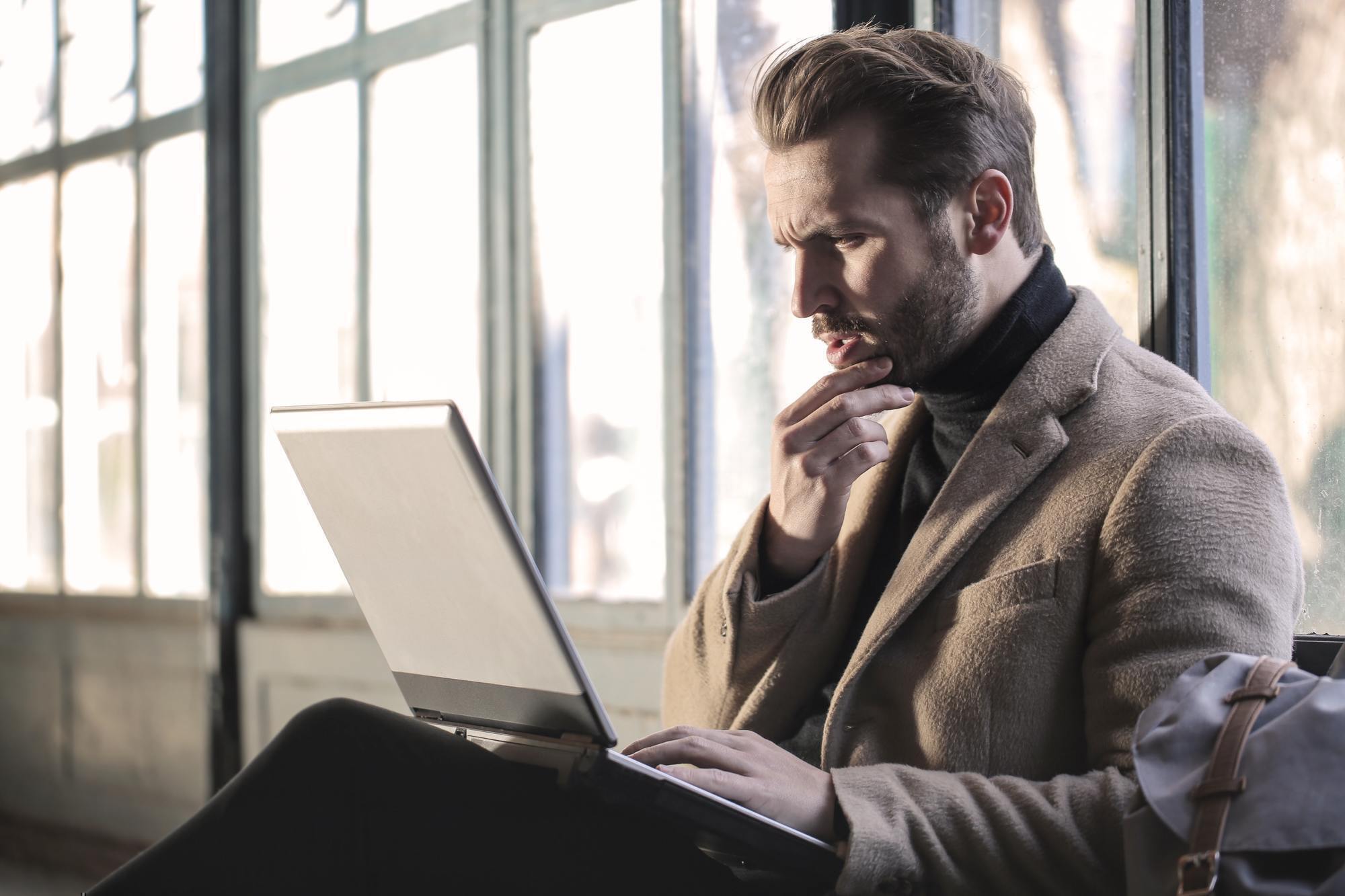 a man rubs his chin as he looks at a computer