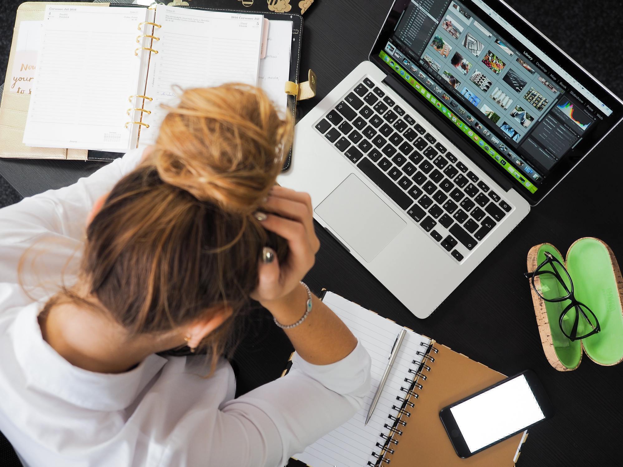 a woman holds her head in her hands while she sits at her desk