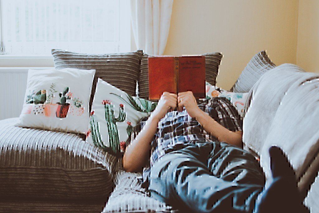 a man reading on a coach with his face covered by the book