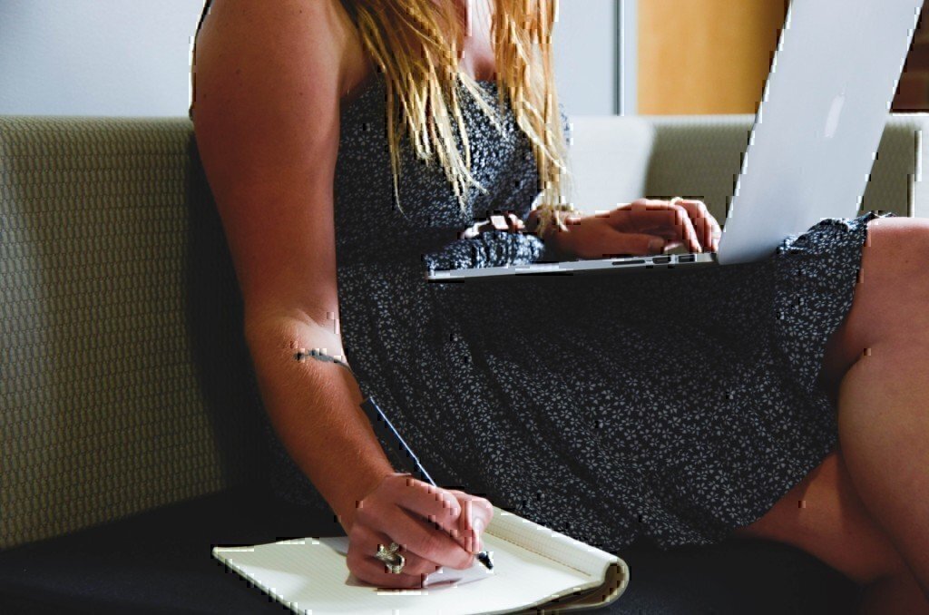 a girl writing on a piece of paper and working on a laptop