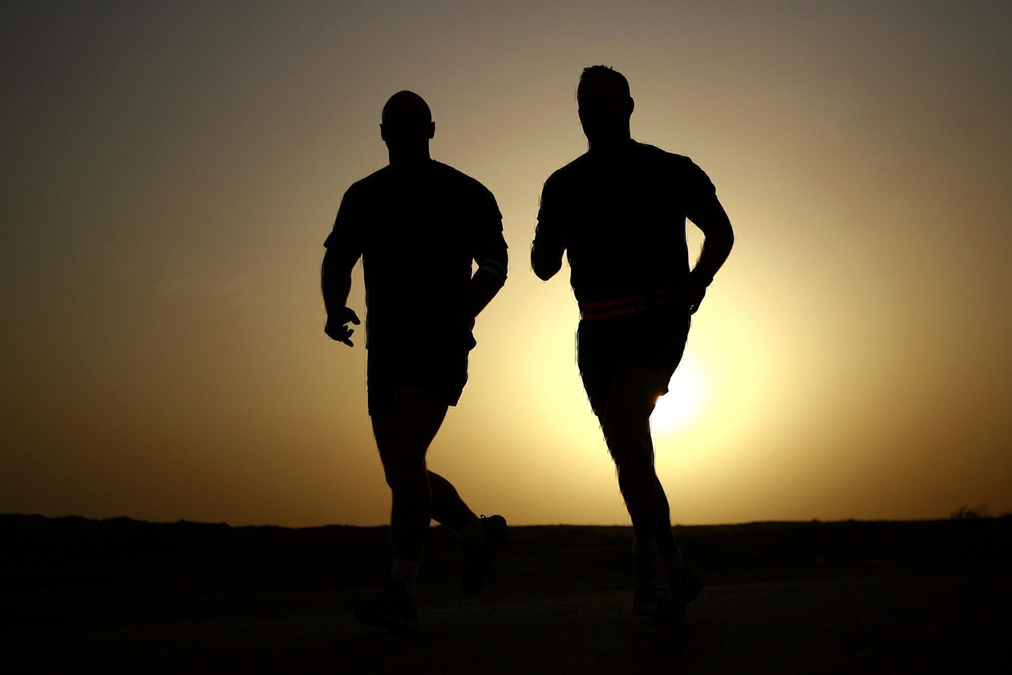 a picture of two guys running in the sunrise