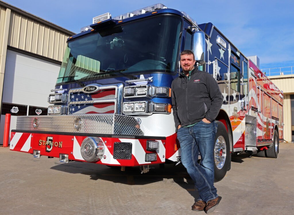 Tom Keddell proudly stands in front of the patriotic firetruck that he made with his new career after the military at Pierce Manufacturing