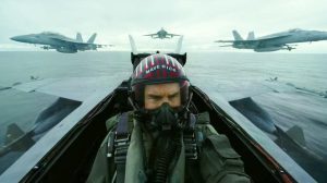 Top Gun 2 Maverick sitting in a fighter plane with other planes in the background.
