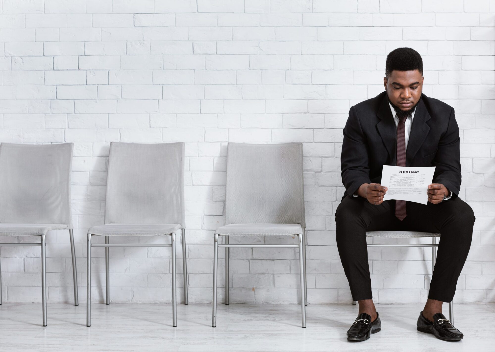 Millennial black man reading his resume while waiting for job interview at office hall, empty space